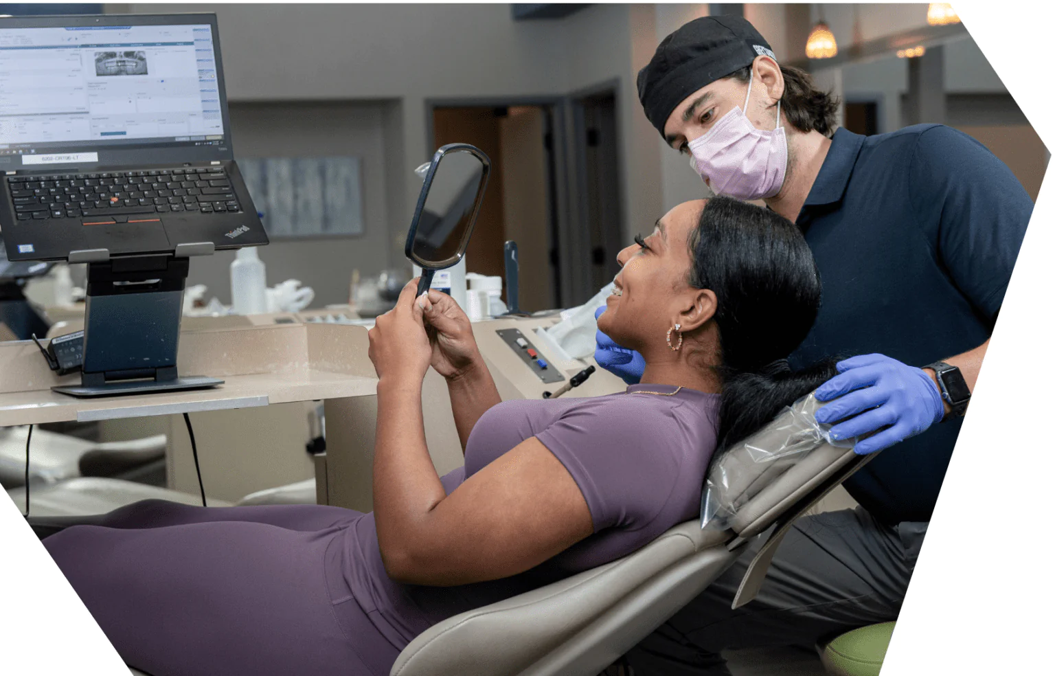 A patient looking at her new braces in a hand mirror while a Werner Orthodontics team member checks the bonding